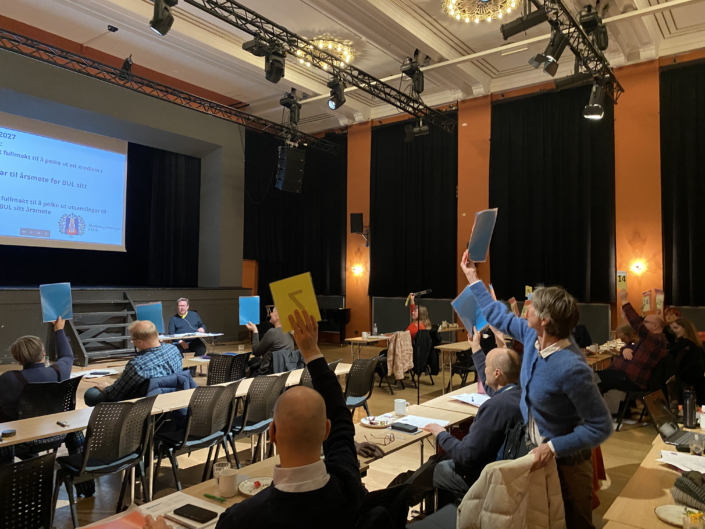 Årsmøte 2026 Møte i stor sal. Menn og kvinner viser stemmeseddel.