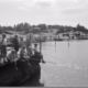 Sommer på Lindøya.Svart- kvitt foto av fire gutar som fiskar på ei brygge. bak står to andre gutar og ein vaksen mann,